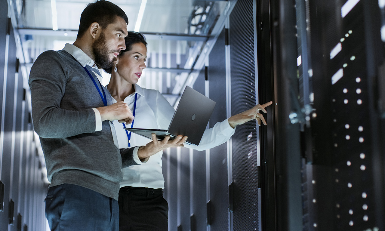 Male IT Specialist Holds Laptop and Discusses Work with Female Server Technician. They're Standing in Data Center, Rack Server Cabinet is Open.